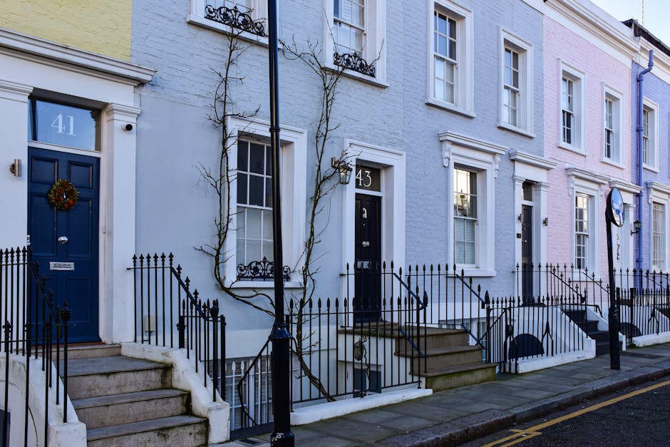 A row of terraced houses on Walthamstow High Street, featuring colorful facades in pastel shades of blue, pink, and cream, each with front steps leading up to black front doors, some decorated with fe