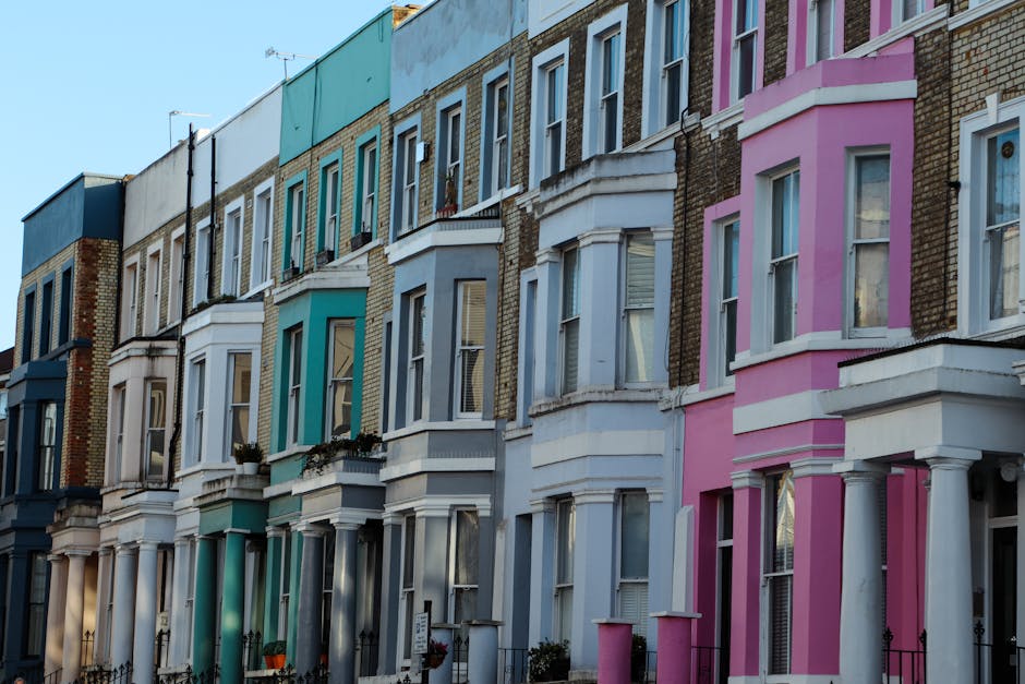 A row of terraced houses on Walthamstow High Street, featuring colorful facades in pastel shades of blue, pink, and cream, each with front steps leading up to black front doors, some decorated with fe